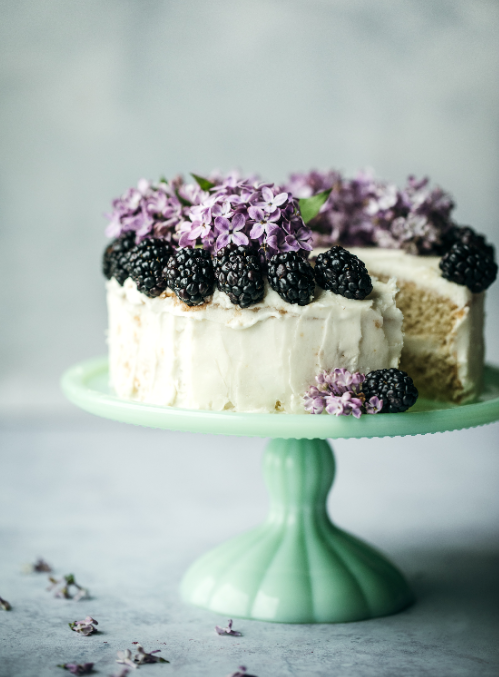 White cake with blackberries decorated on top, sitting on a green cake stand.