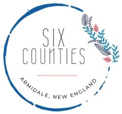 Six Counties logo - blue coffee cup stain with floral accent, around the words SIX COUNTIES Armidale, New England