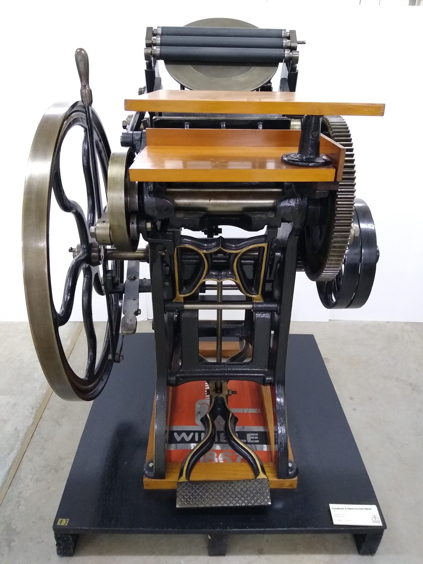 Cast iron printing press with ornate flywheel, treadle, and timber feed boards