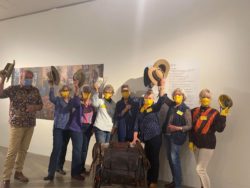 the packsaddle committee stand in front of the opening to the exhibition wearing yellow gloves and masks, and tipping their akubras