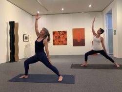 Two women in matching yoga poses within art gallery