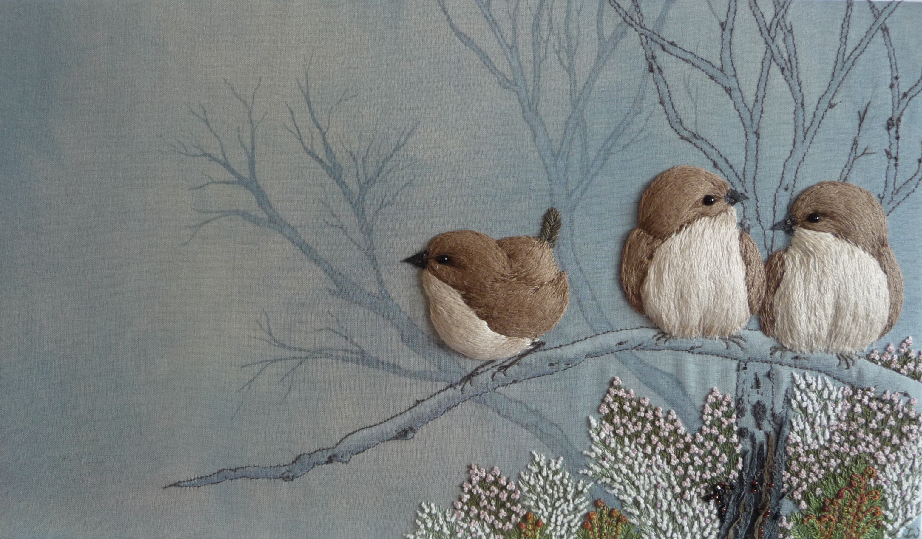 Embroidered image of three small birds on a branch