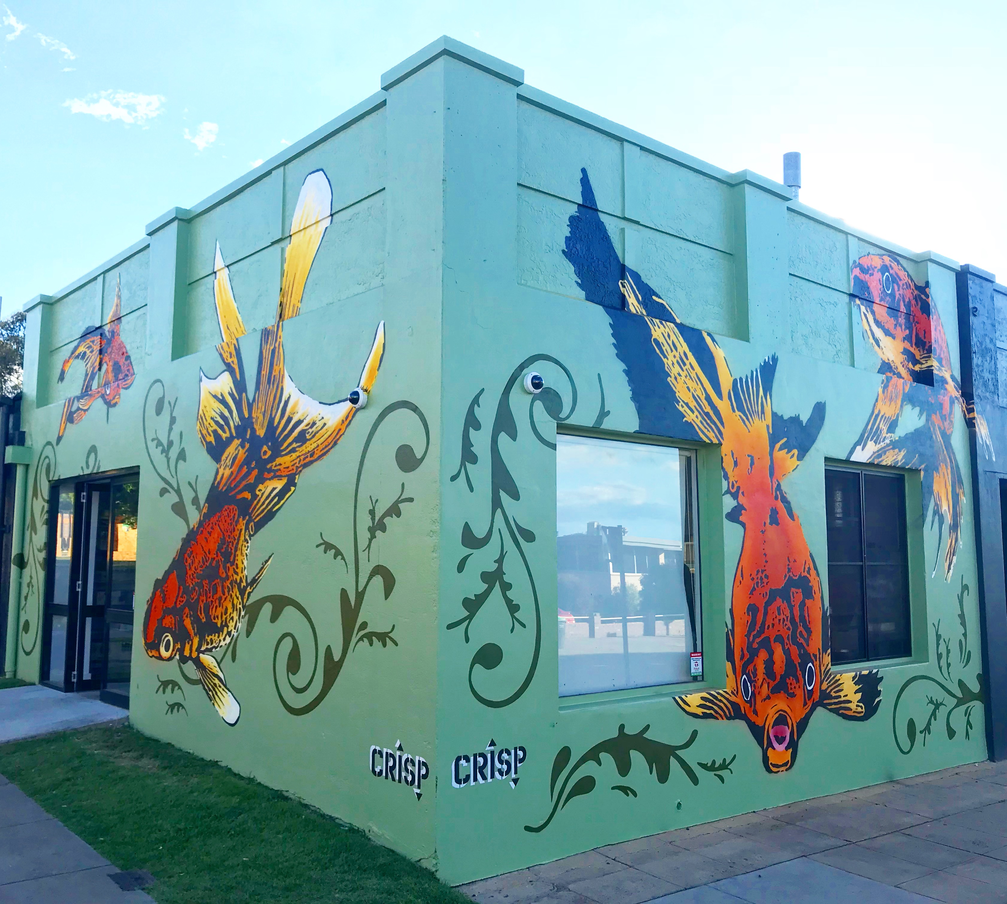 Corner building featuring mural of large goldfish and ornamental designs on green background