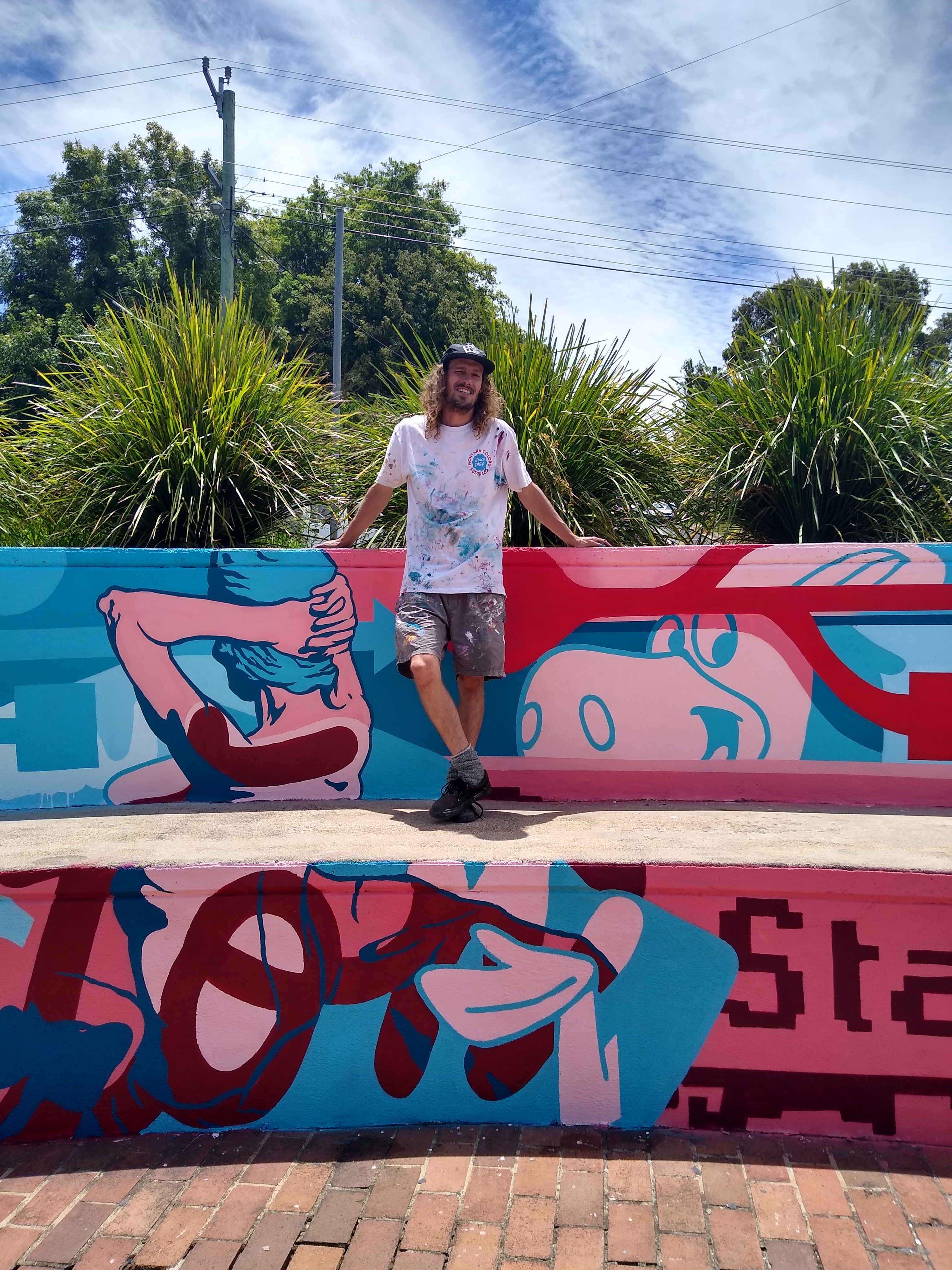 Young man with long hair standing on the whisper wall outside NERAM, featuring a graffiti mural