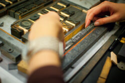Pair of hands arranging lead type in a frame that already contains wood type.